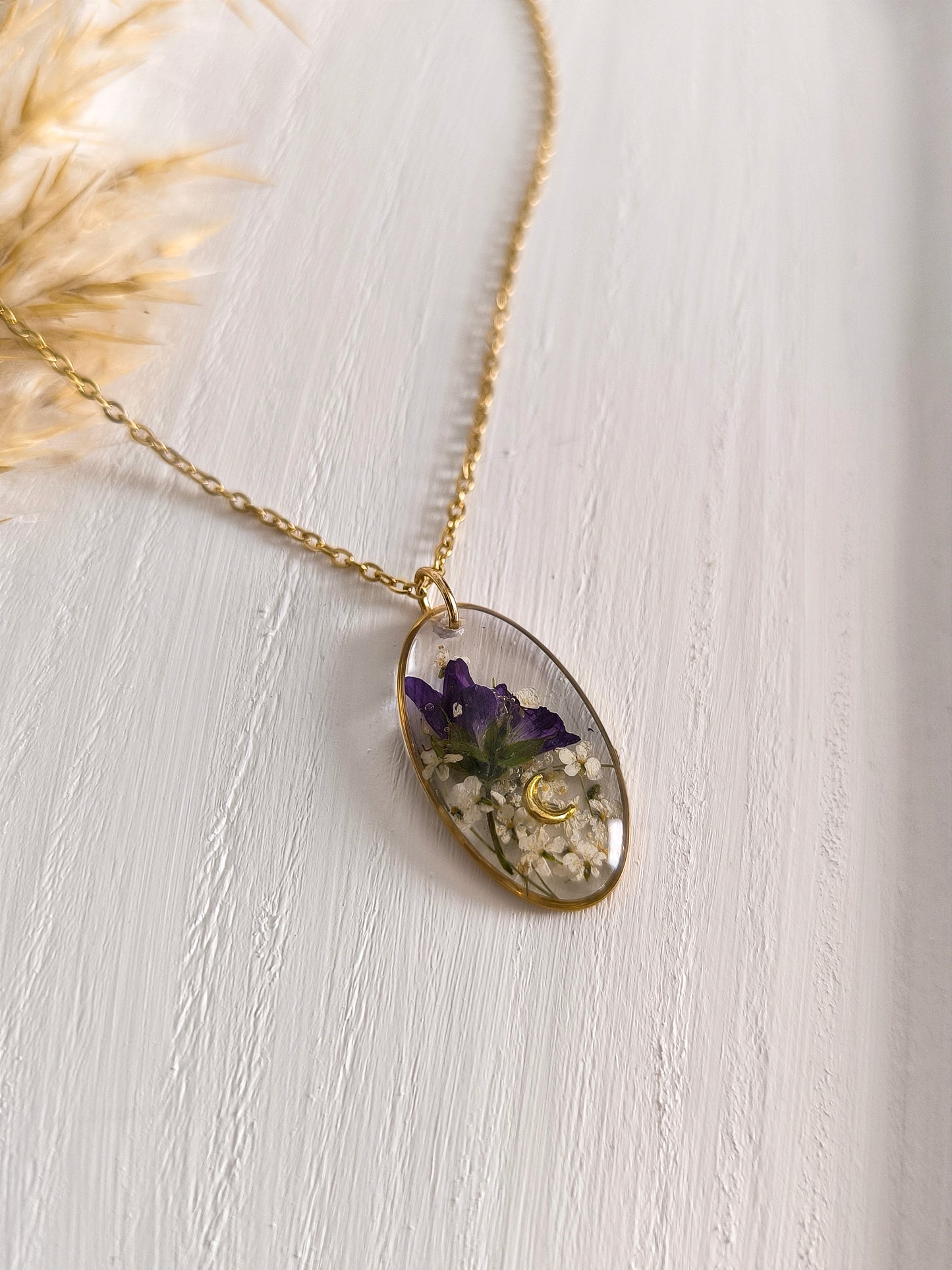 Collier médaillon ovale composé de fleurs séchées encapsulées dans une résine transparente.
