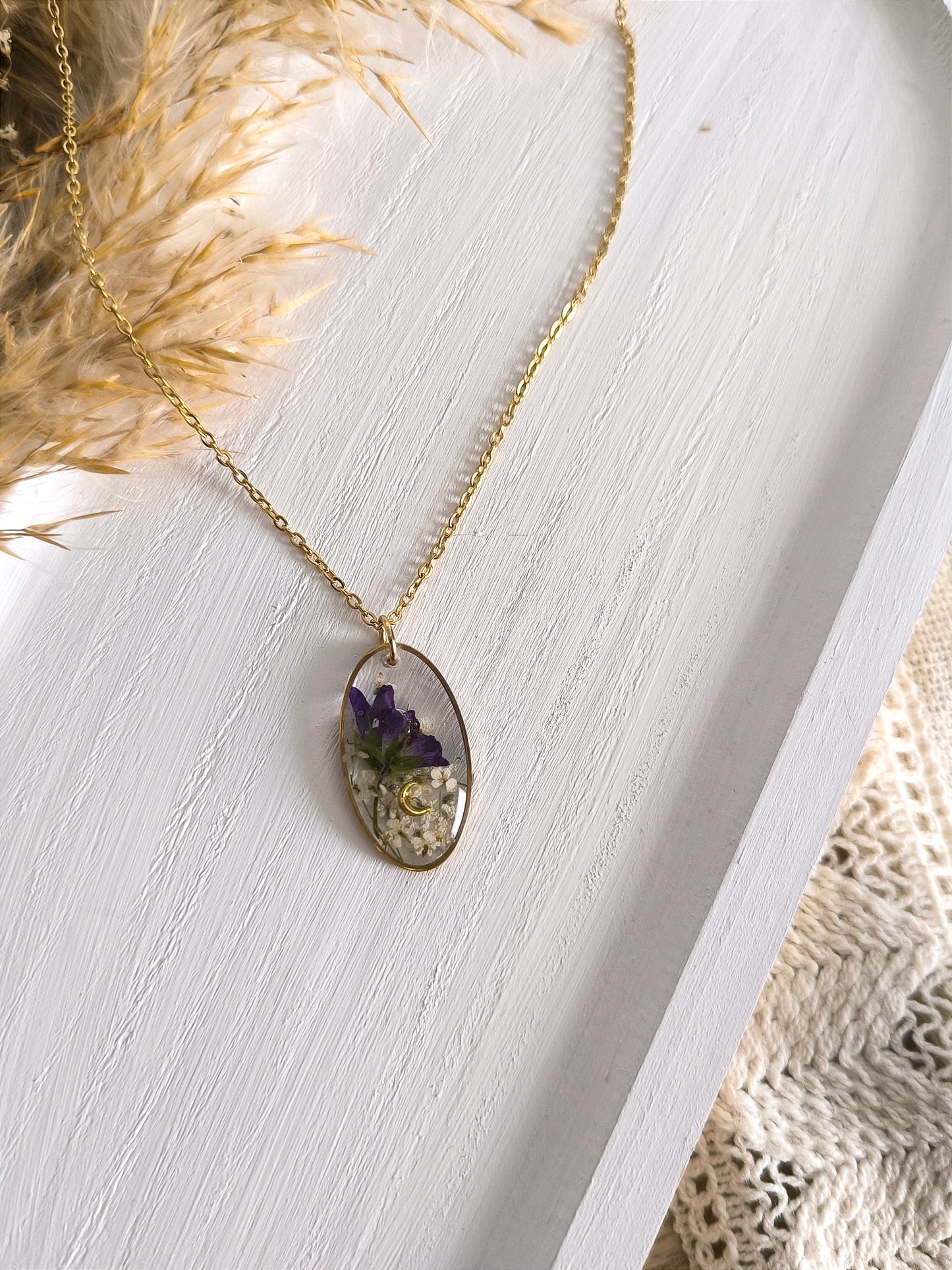 Collier médaillon ovale composé de fleurs séchées encapsulées dans une résine transparente.