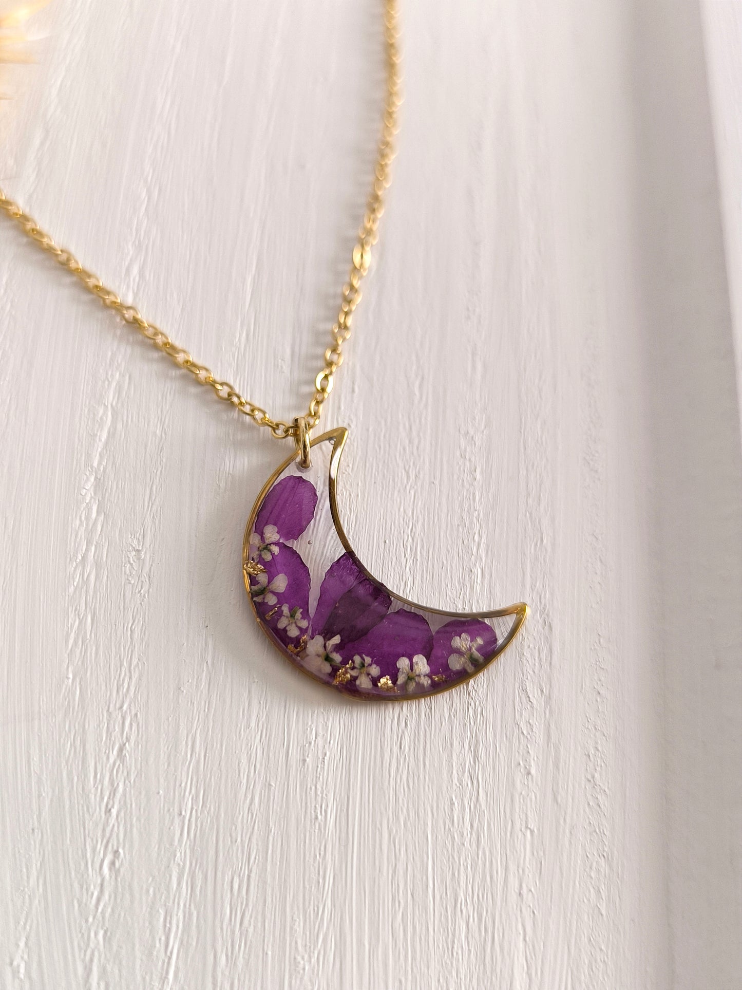 Collier médaillon lune rempli de fleurs séchées glacées dans une résine transparente.