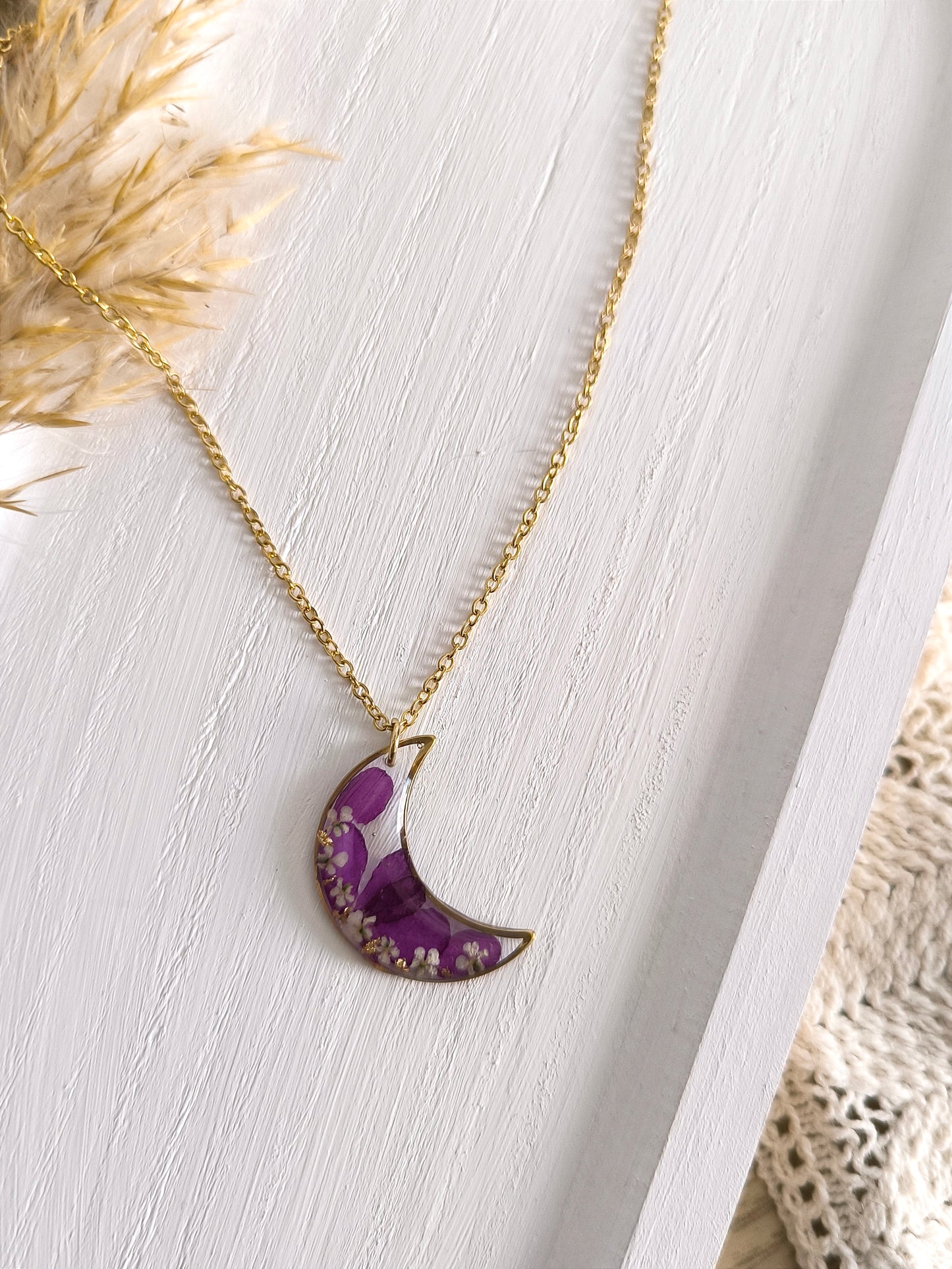 Collier médaillon lune rempli de fleurs séchées glacées dans une résine transparente.