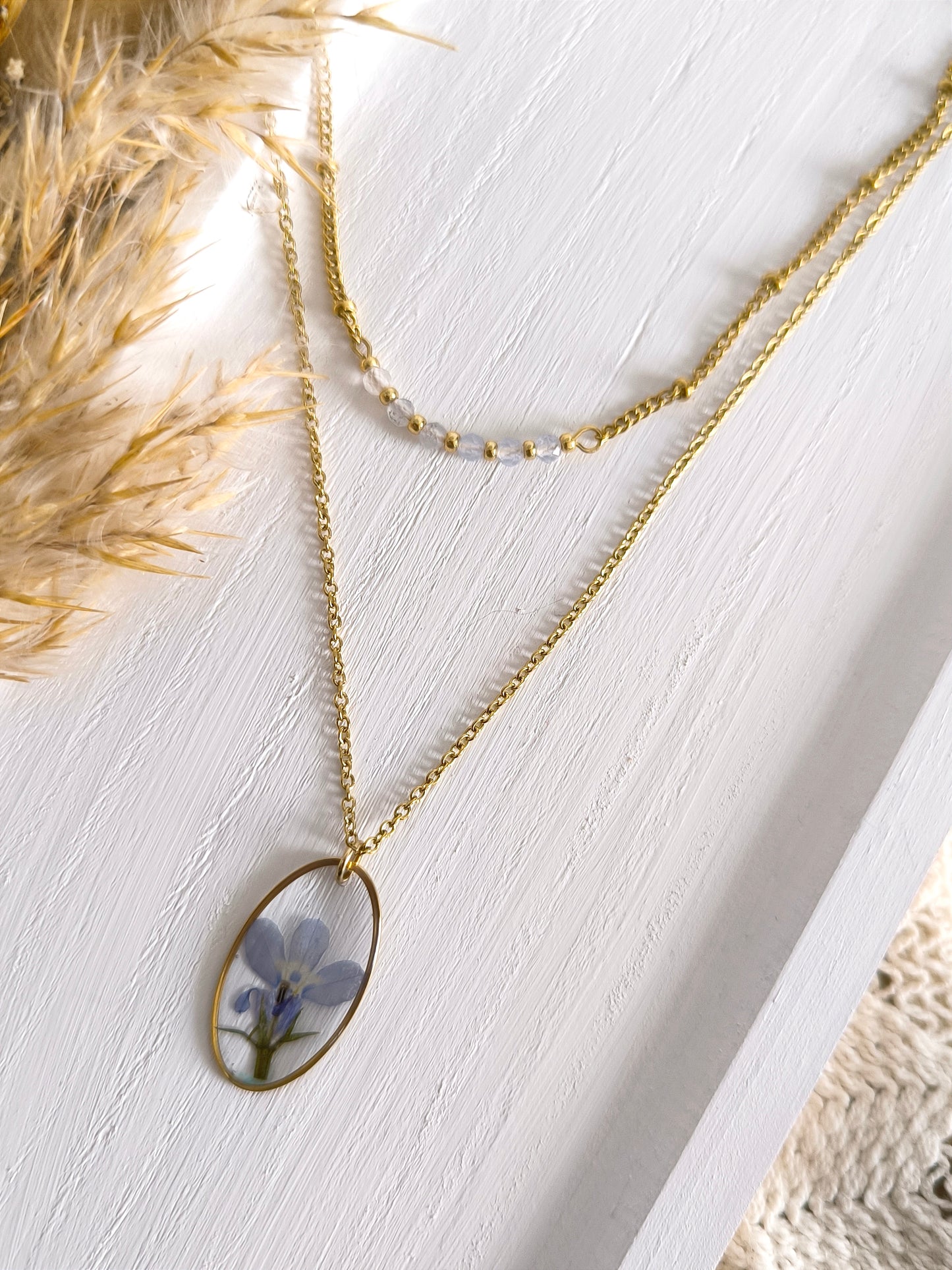 Duo de colliers composés de pierre de calcédoine bleue, d'une fleur séchée de lobélie et d'acier doré.