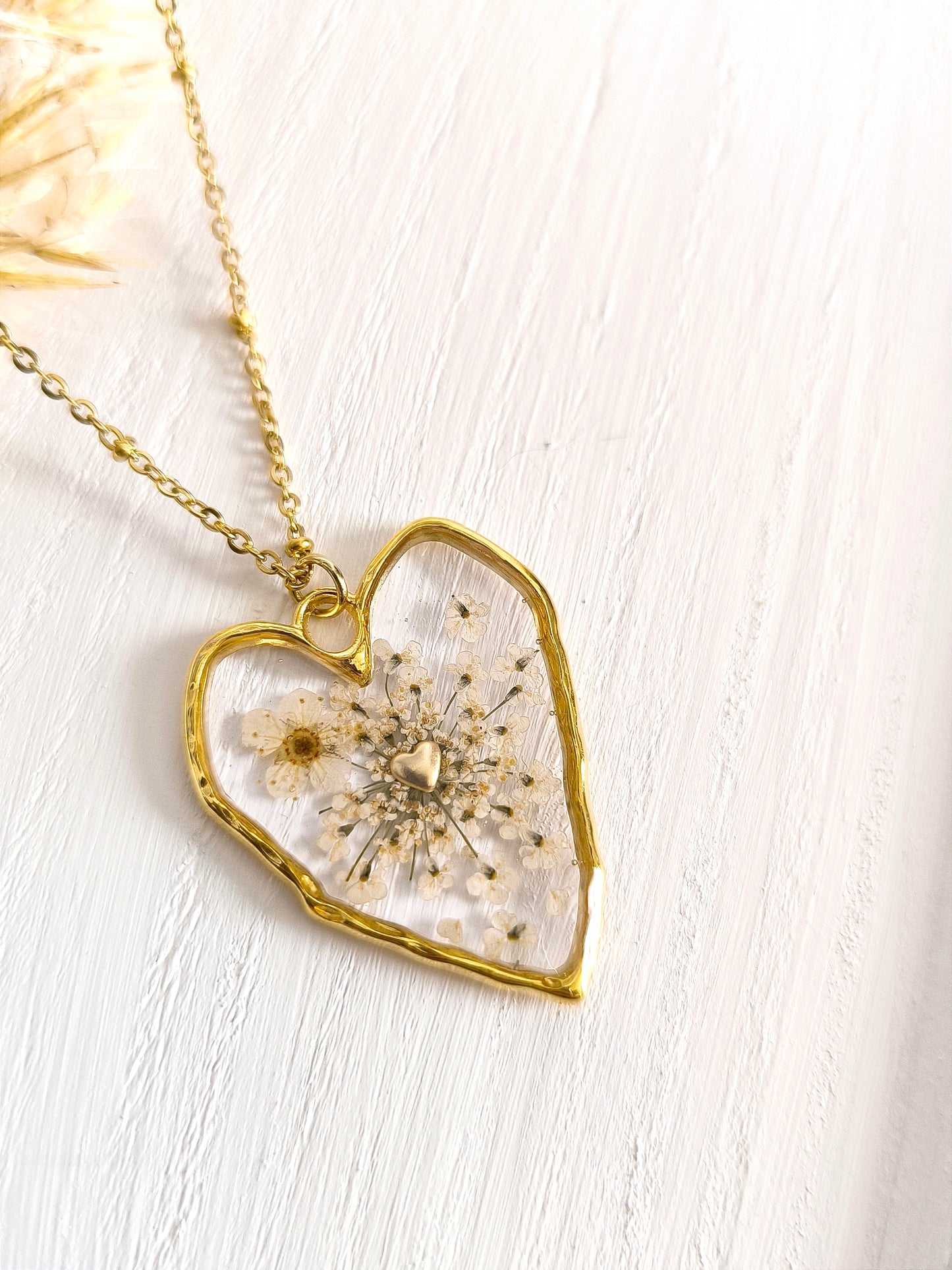Collier bohème en forme de cœur, rempli de fleurs blanches encapsulées dans une résine transparente.