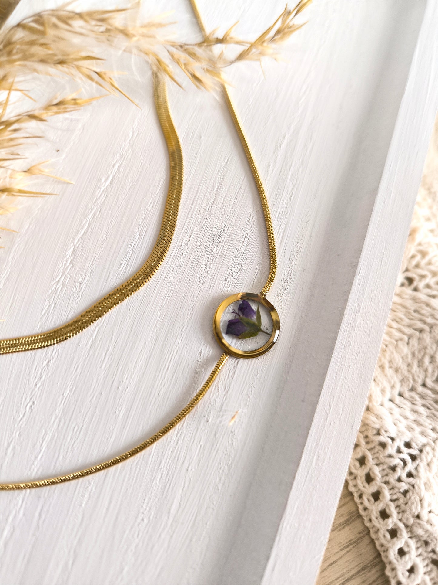 Duo de colliers en acier doré et fleurs séchée encapsulée dans une résine transparente.