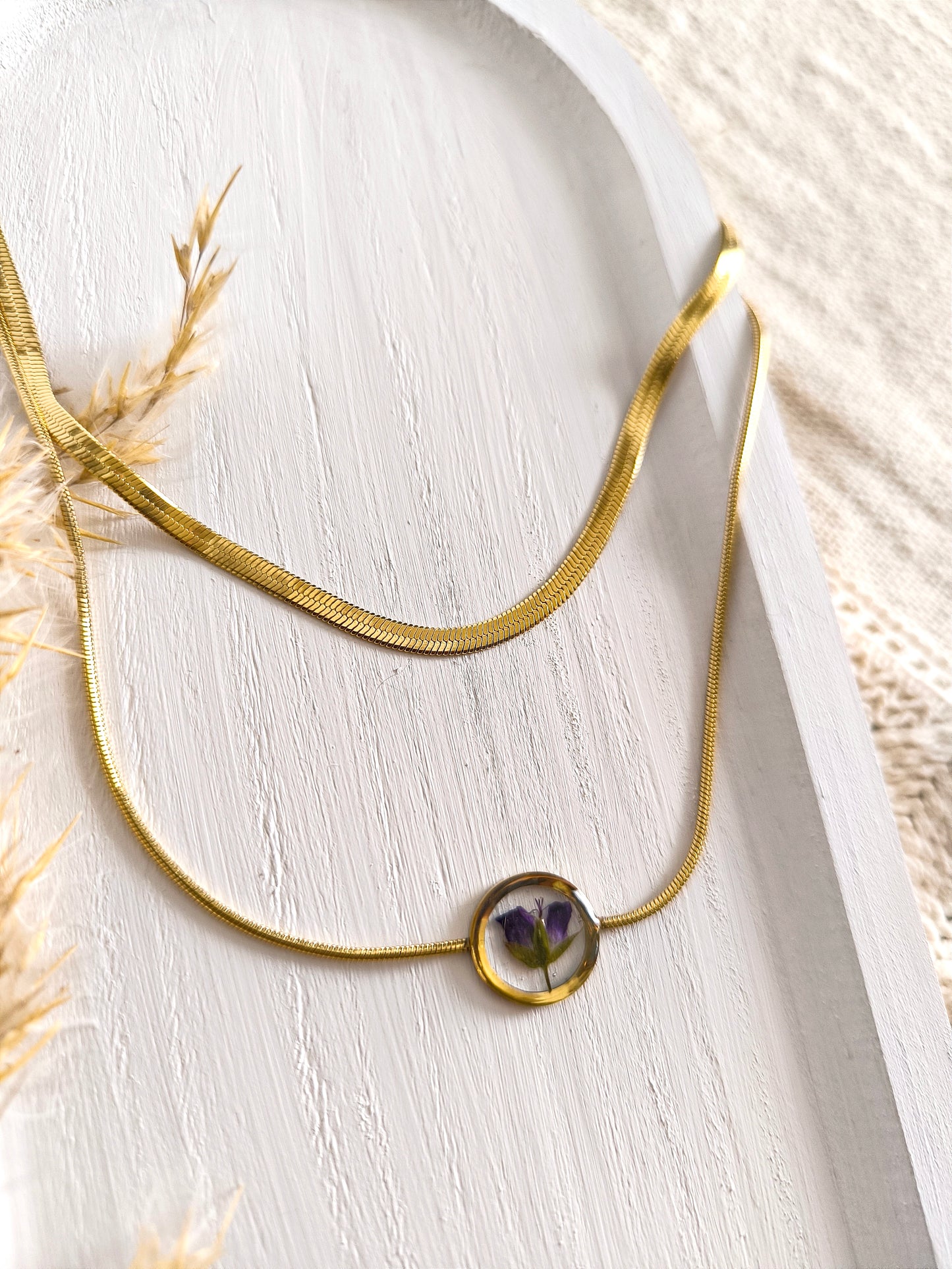 Duo de colliers en acier doré et fleurs séchée encapsulée dans une résine transparente.