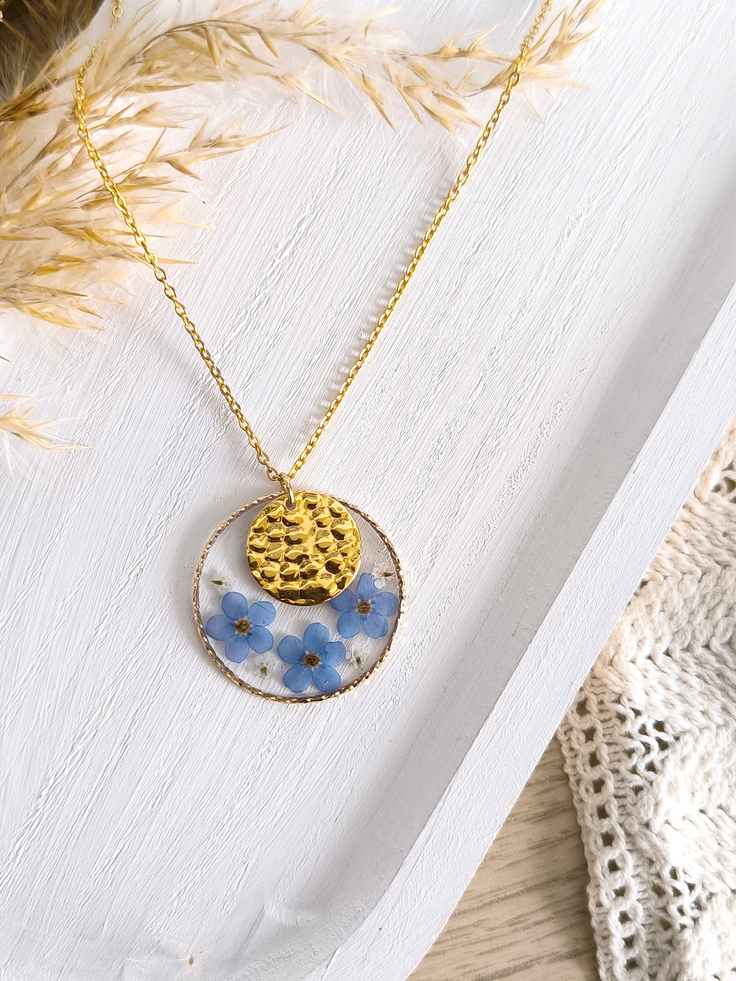 Collier sautoir en acier doré composé de fleurs pressées et séchées encapsulées dans une résine transparente.