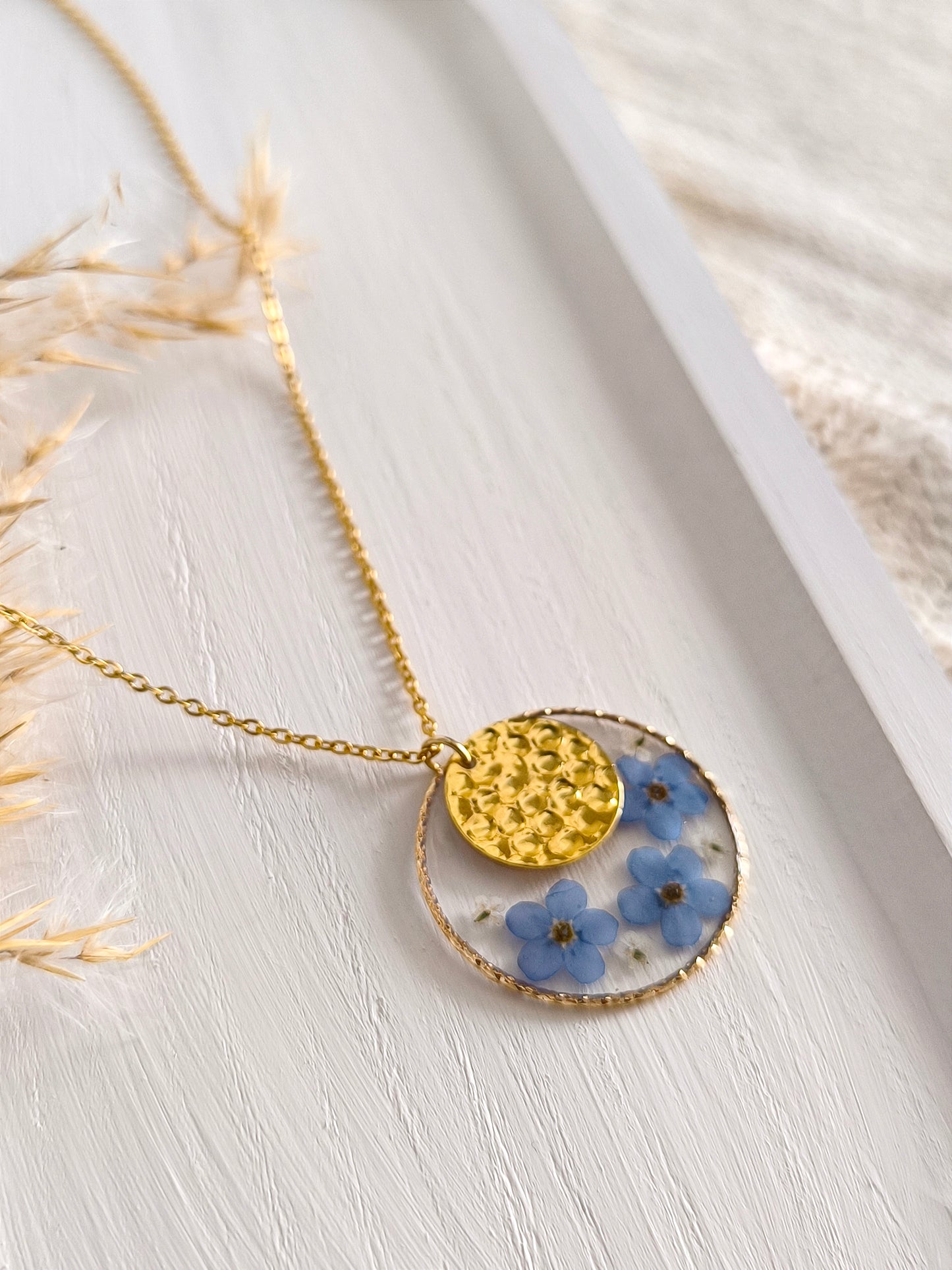 Collier sautoir en acier doré composé de fleurs pressées et séchées encapsulées dans une résine transparente.
