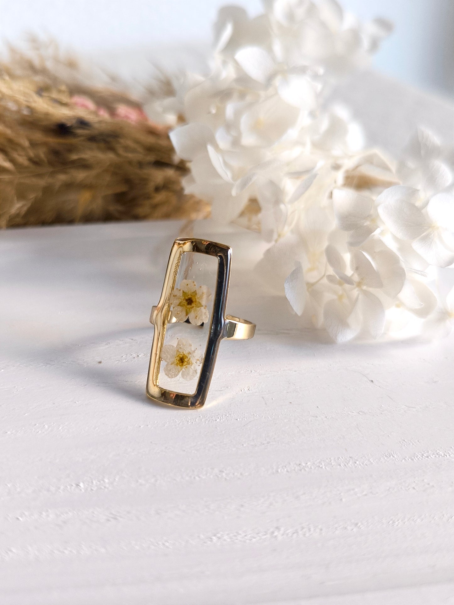 Bagues en acier doré avec fleurs séchée encapsulée dans une résine transparente.