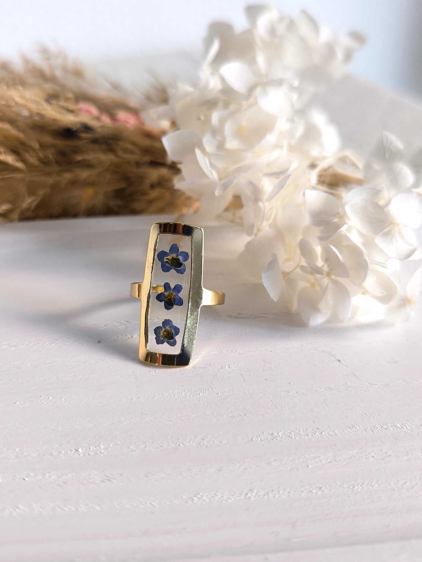 Bagues en acier doré avec fleurs séchée encapsulée dans une résine transparente.
