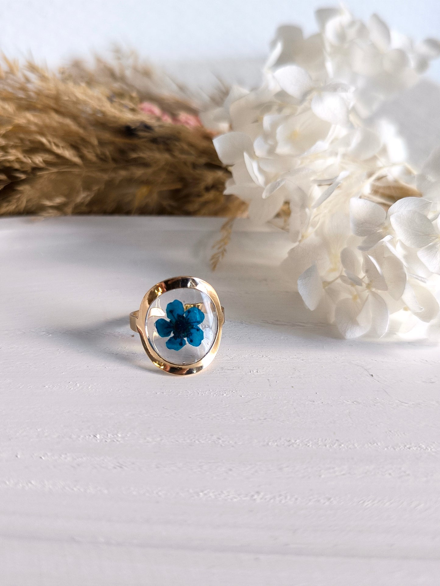 Bagues en acier doré avec fleurs séchée encapsulée dans une résine transparente.