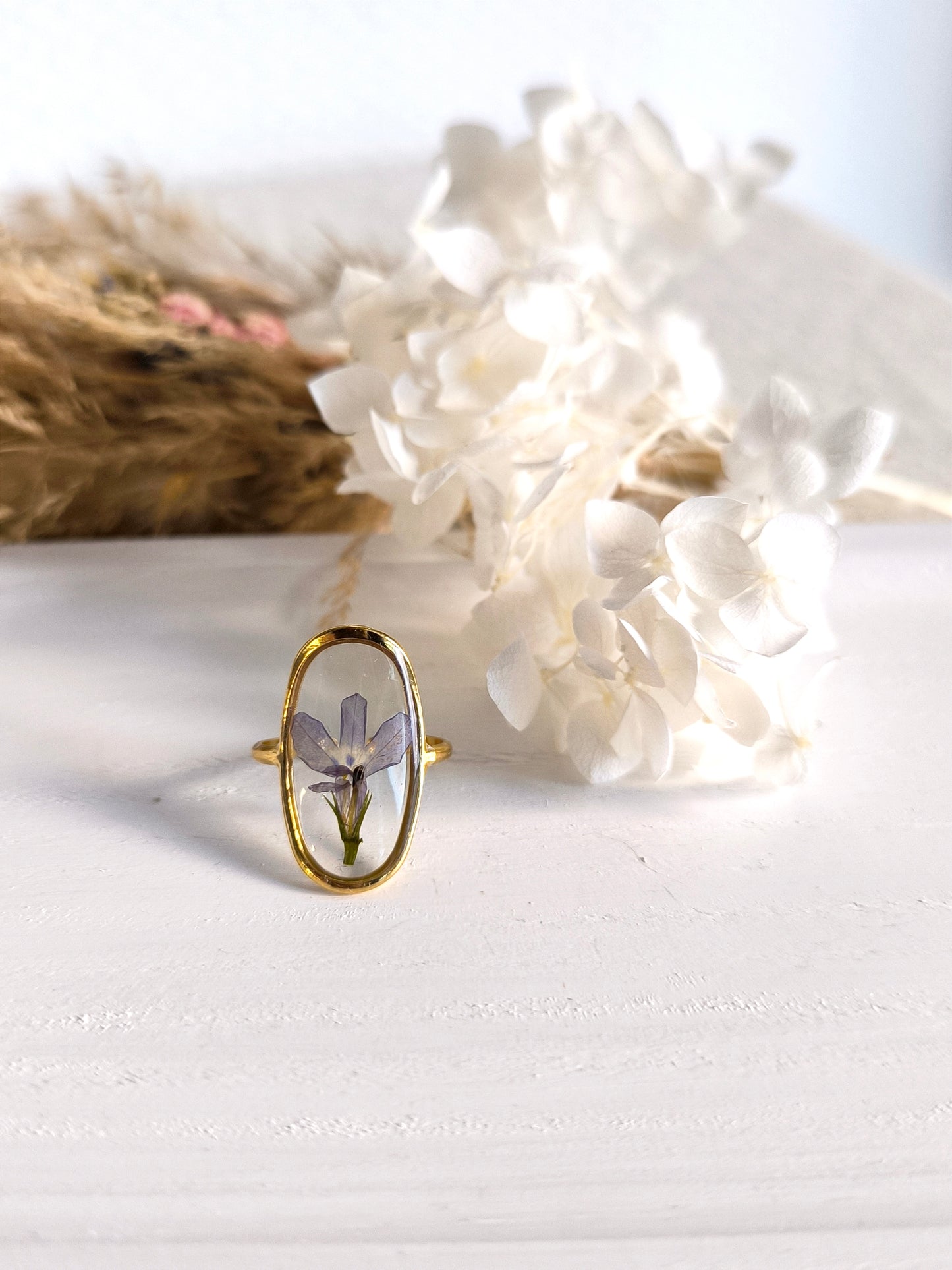 Bagues en acier doré avec fleurs séchée encapsulée dans une résine transparente.