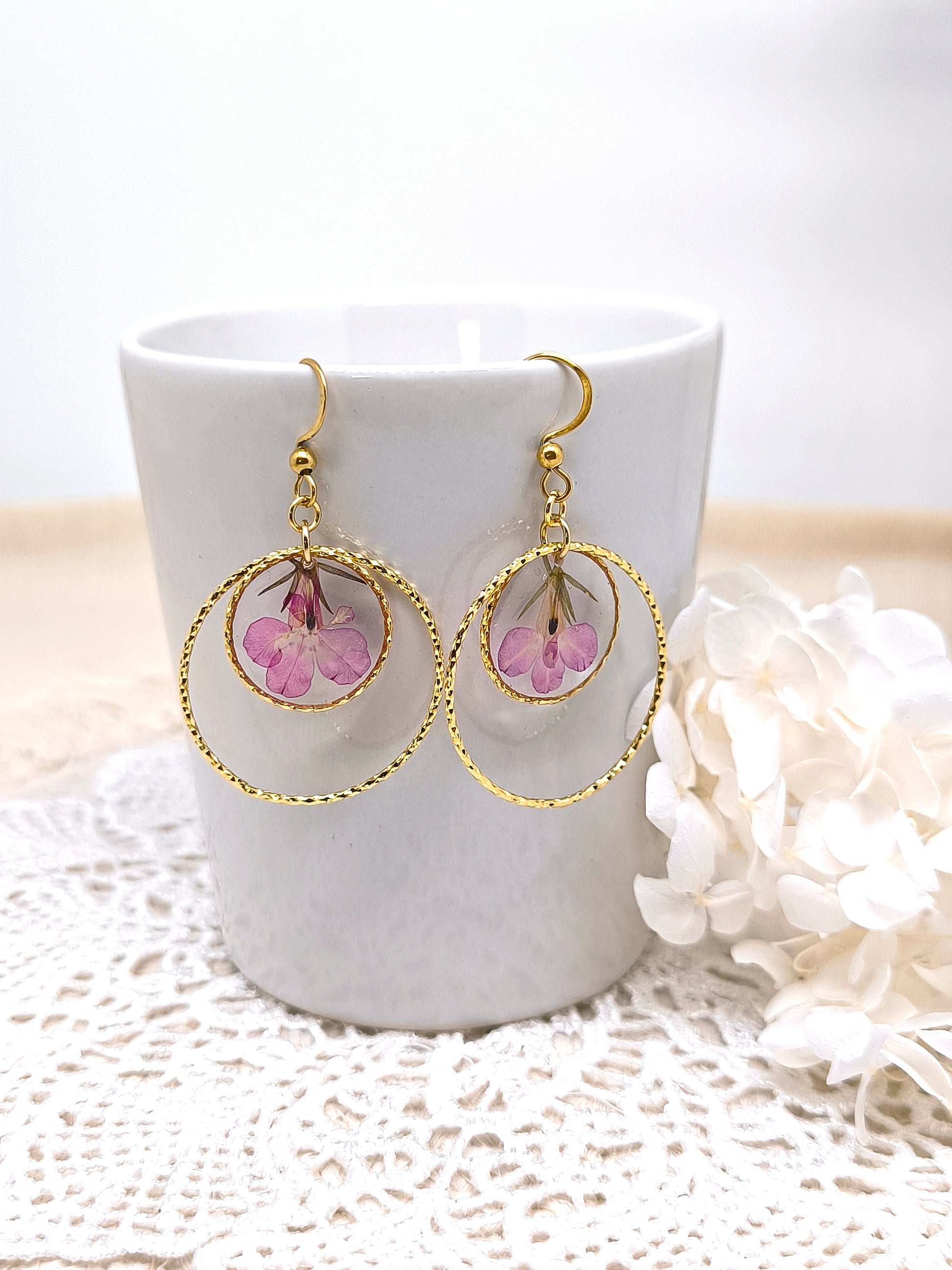 Boucles d'oreilles rondes avec fleur de lobélie encapsulée dans une résine transparente.