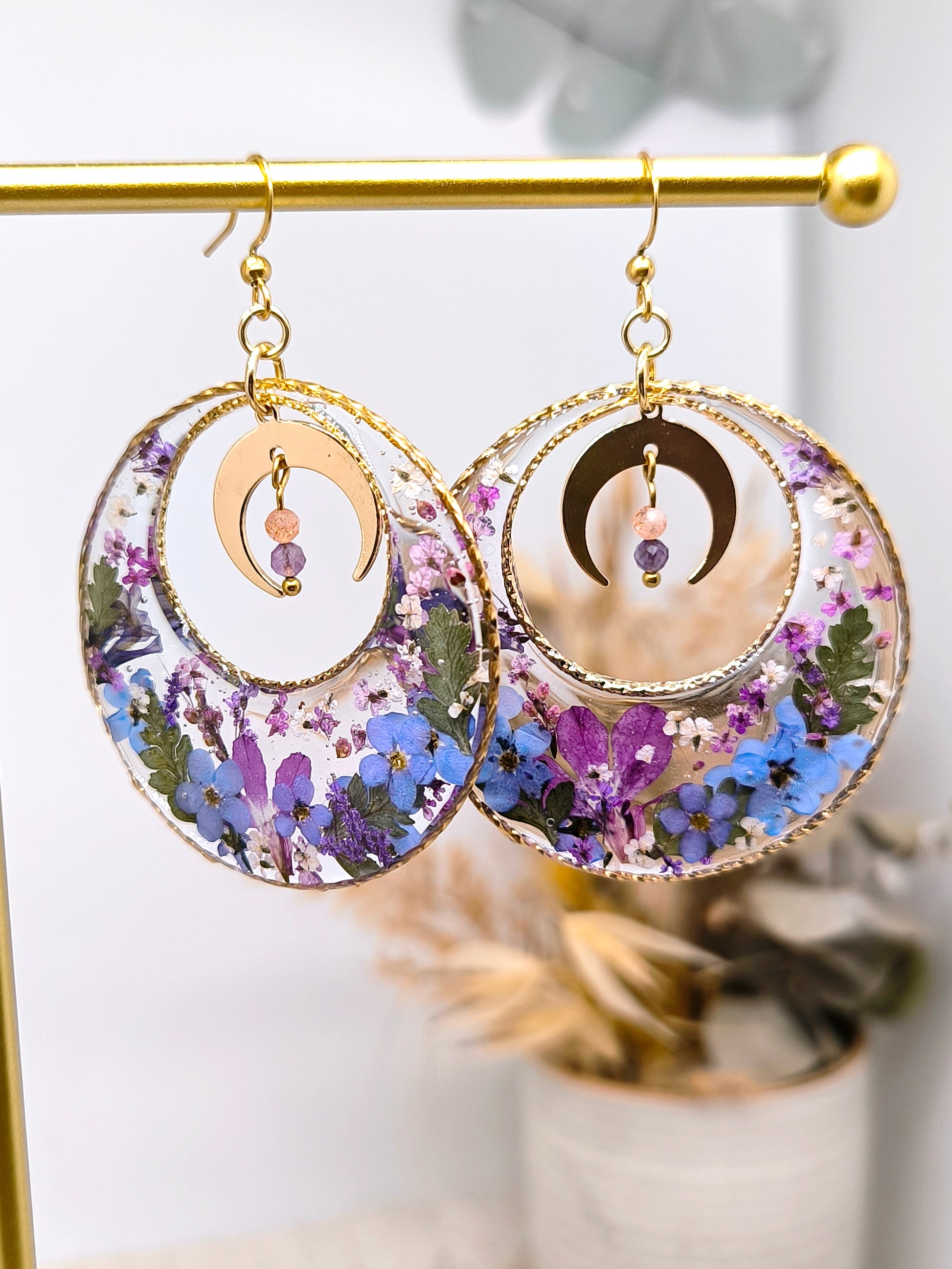 Boucles d'oreilles maxi créoles lunaires composées de fleurs séchées encapsulées dans une résine transparente.