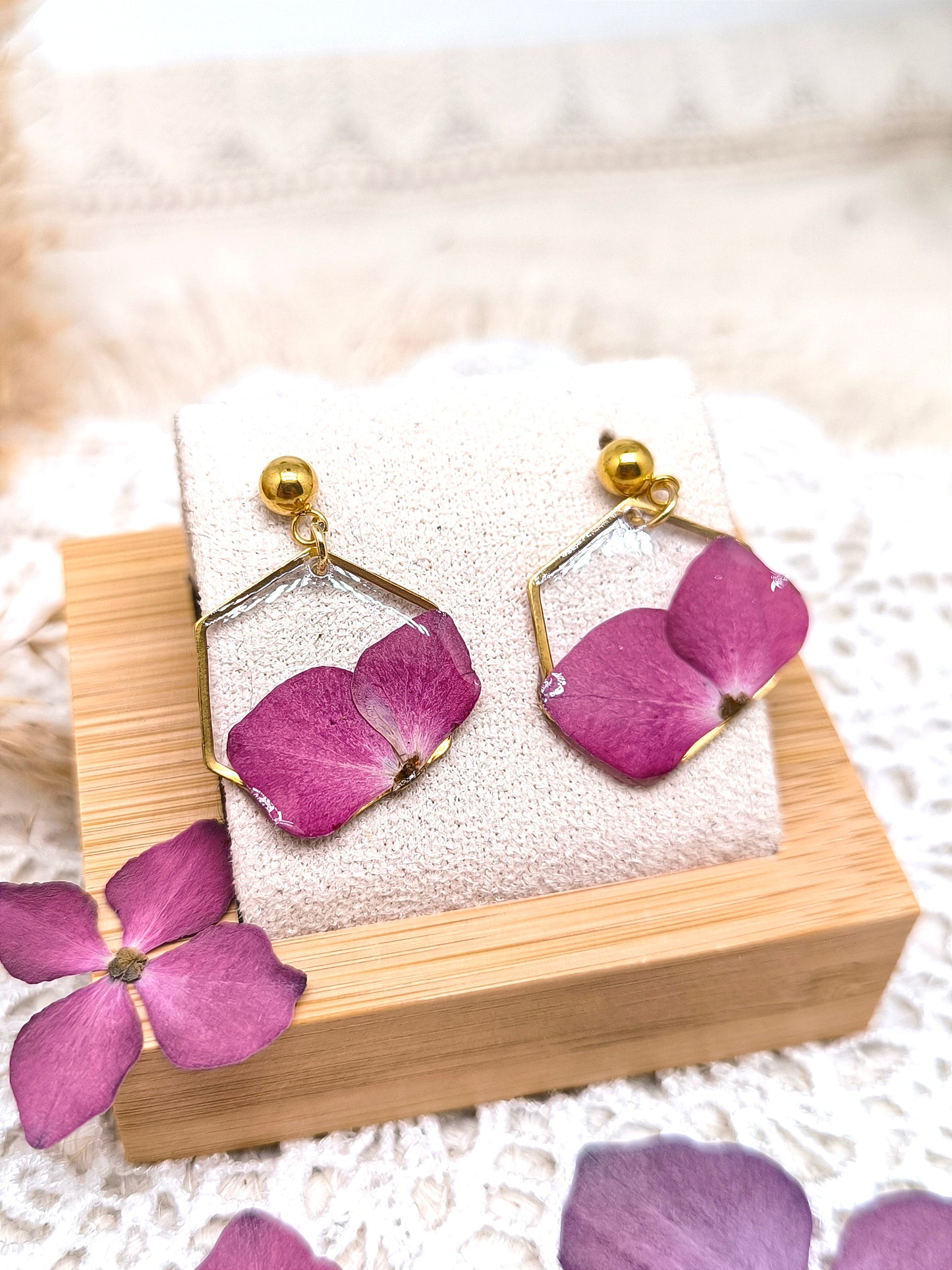 Boucles d'oreilles puces, renfermant dans son cadre des pétales de fleurs d'hortensia rose encapsulées dans une résine transparente.