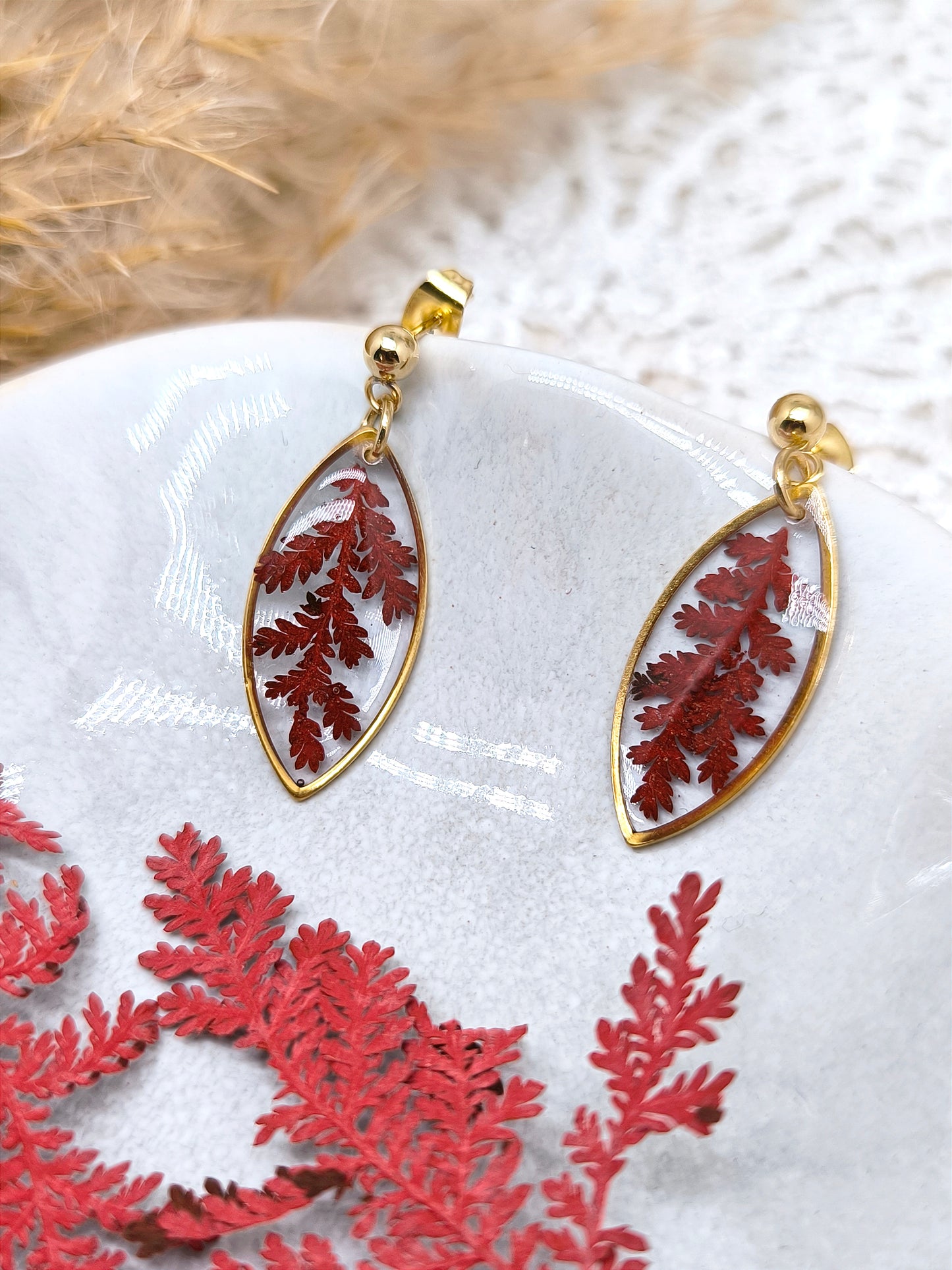 Boucles d'oreilles en forme de navette avec fougère rouge séchée et résine transparente.