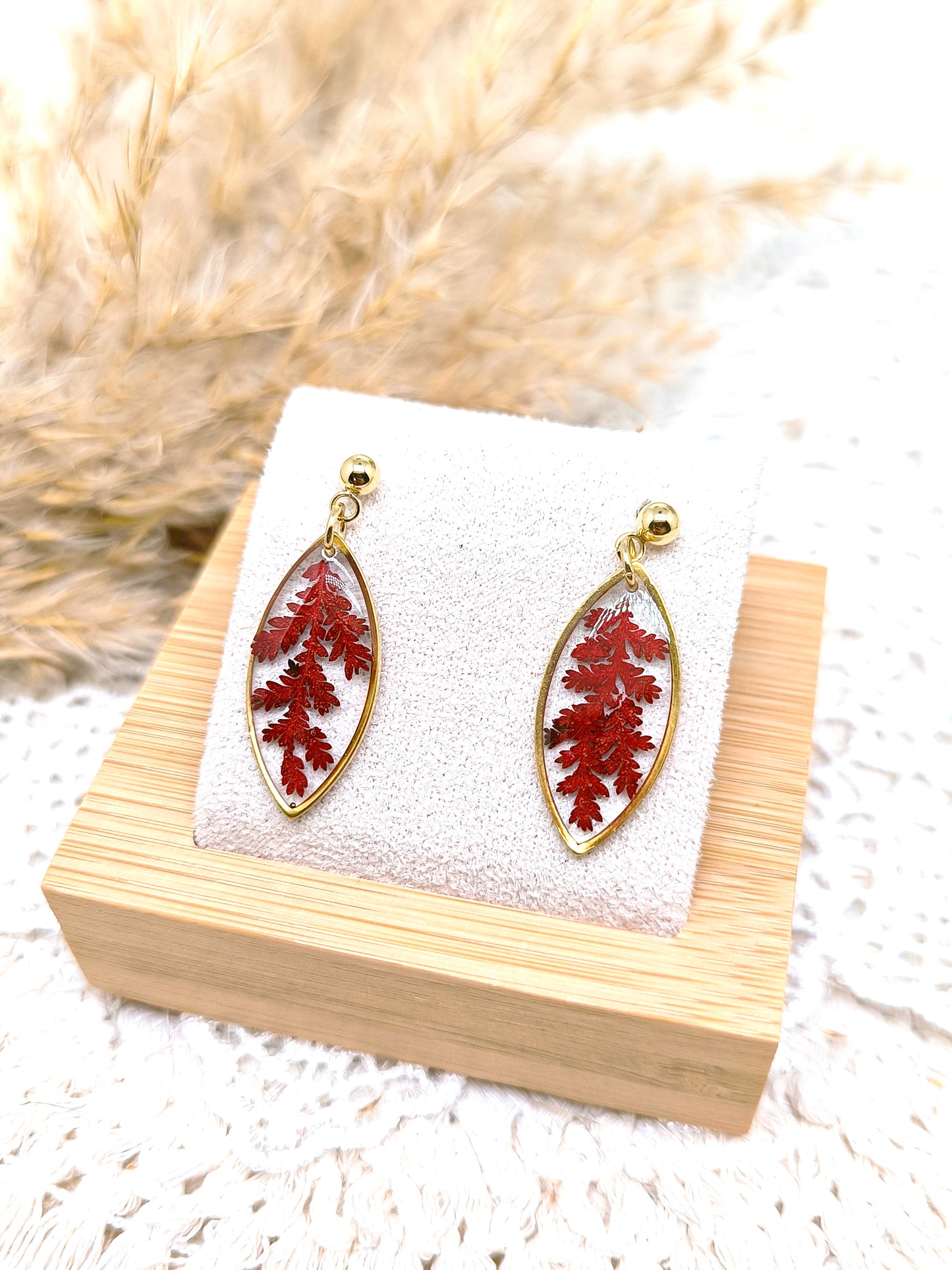 Boucles d'oreilles en forme de navette avec fougère rouge séchée et résine transparente.