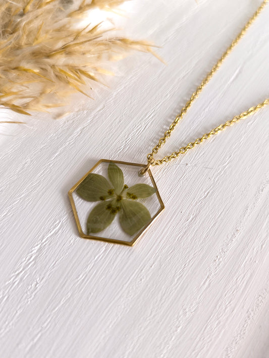 Collier médaillon hexagone rempli de fleurs séchées glacées dans une résine transparente.