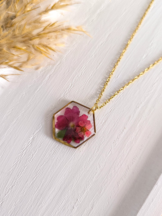 Collier médaillon hexagone rempli de fleurs séchées glacées dans une résine transparente.