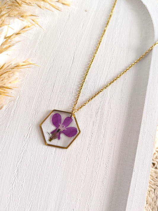 Collier médaillon hexagone rempli de fleurs séchées glacées dans une résine transparente.