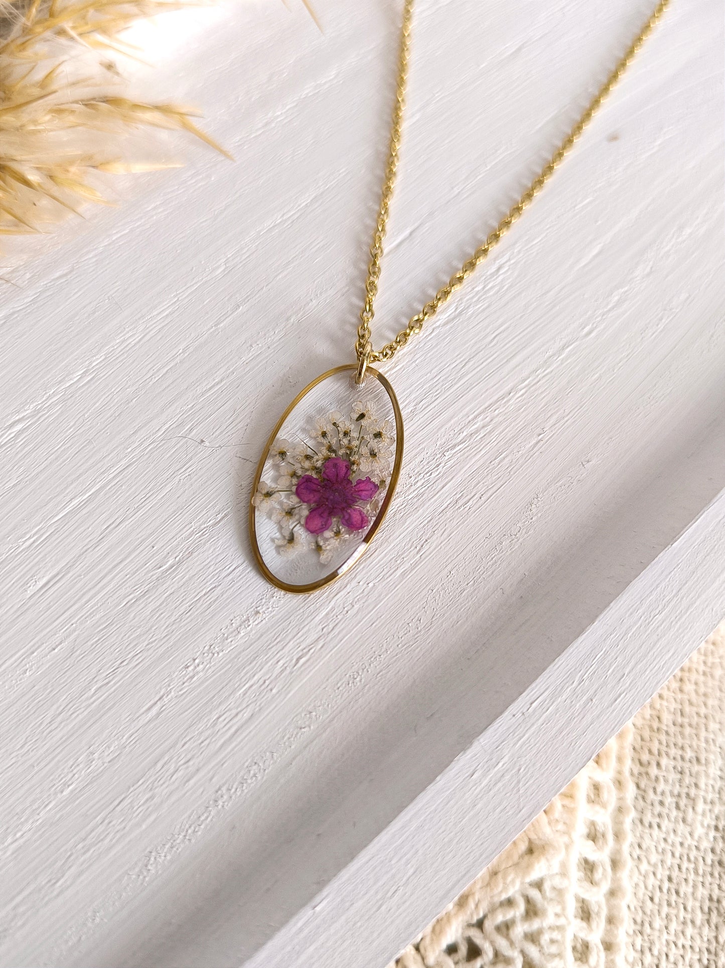 Collier médaillon ovale rempli de fleurs séchées glacées dans une résine transparente.