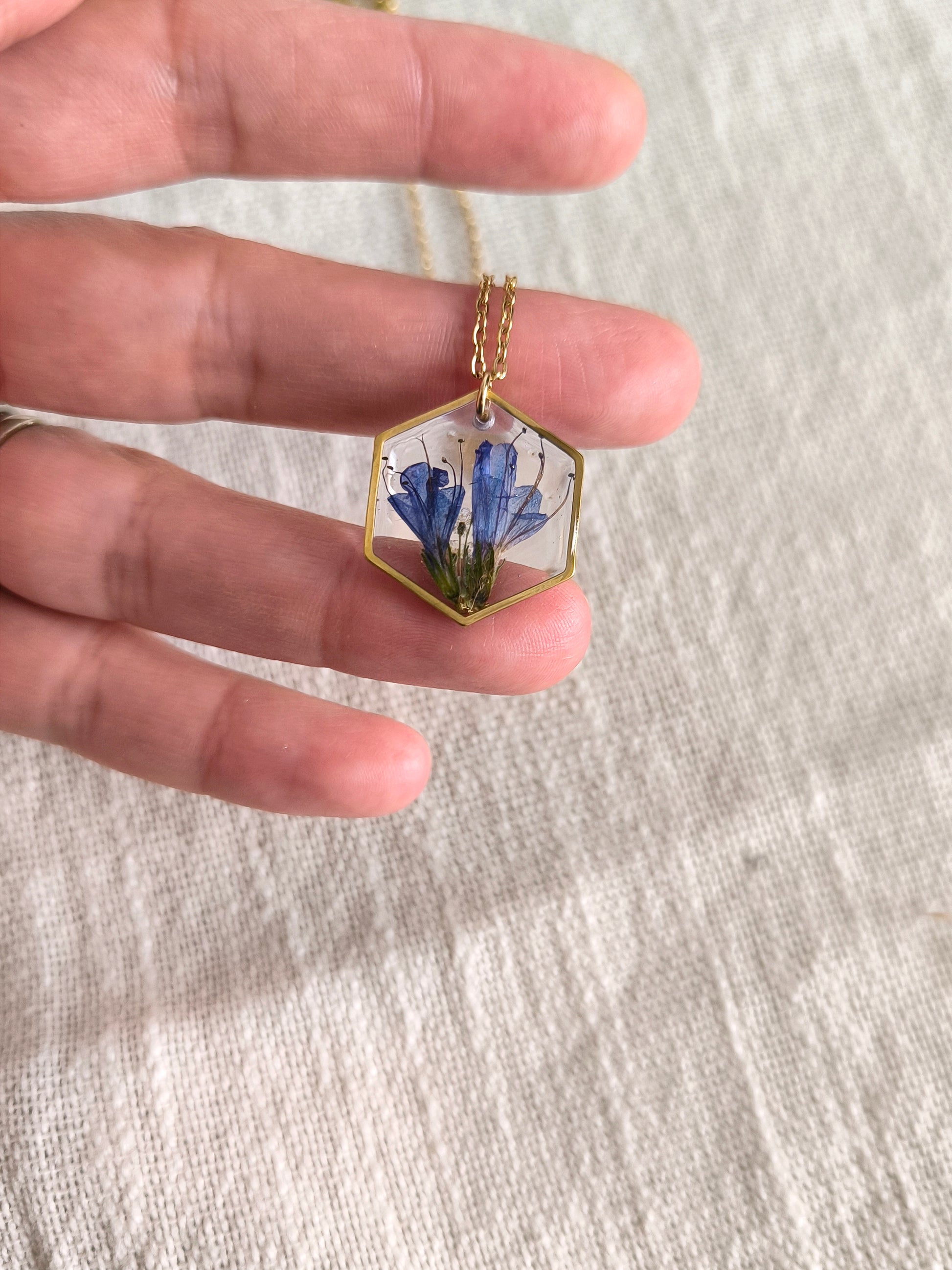 Collier médaillon hexagone rempli de fleurs séchées glacées dans une résine transparente.