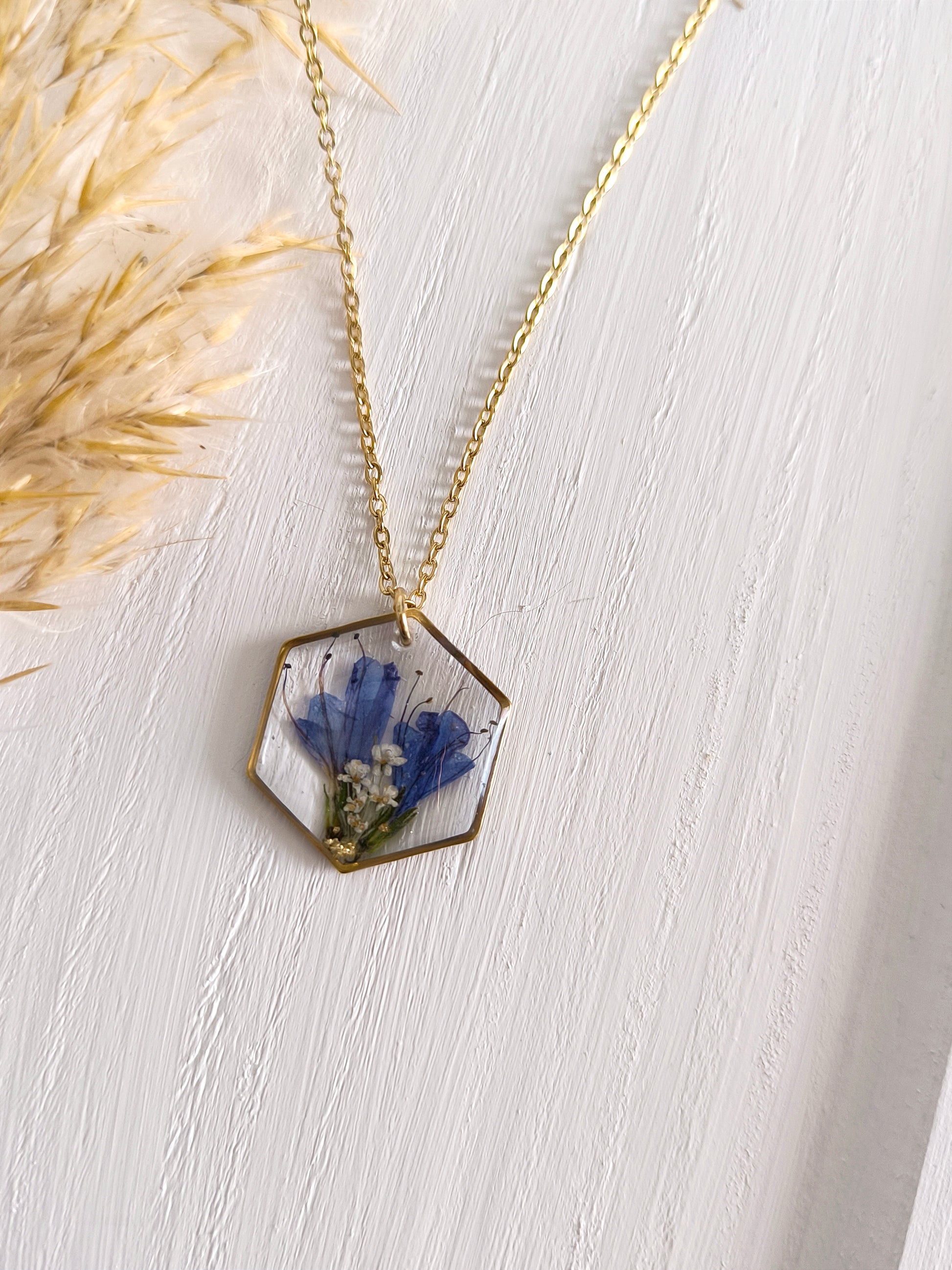 Collier médaillon hexagone rempli de fleurs séchées glacées dans une résine transparente.