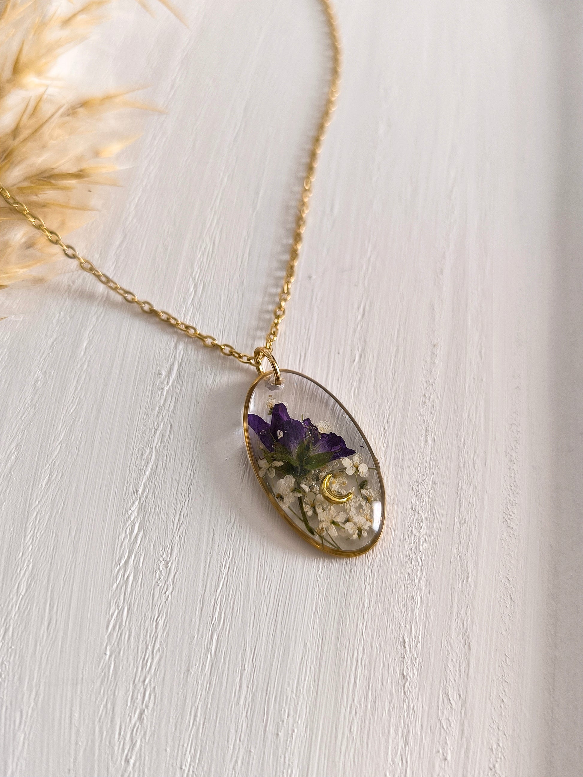 Collier médaillon ovale composé de fleurs séchées encapsulées dans une résine transparente. 