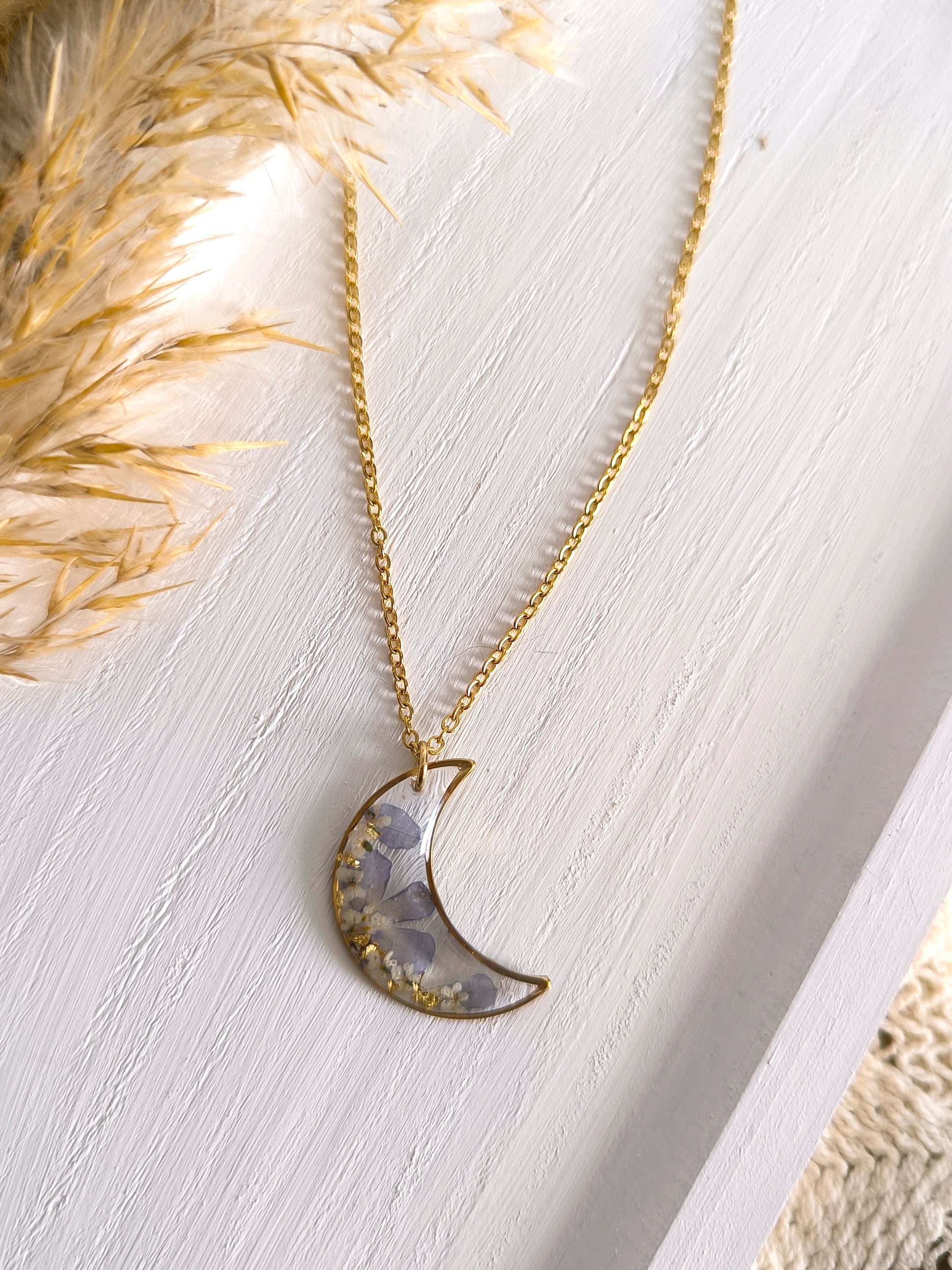 Collier médaillon lune rempli de fleurs séchées glacées dans une résine transparente. 