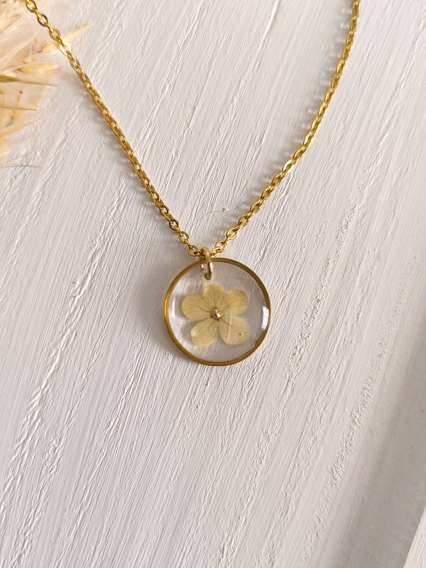 Collier médaillon rond soliflore rempli de fleurs séchées glacées dans une résine transparente.