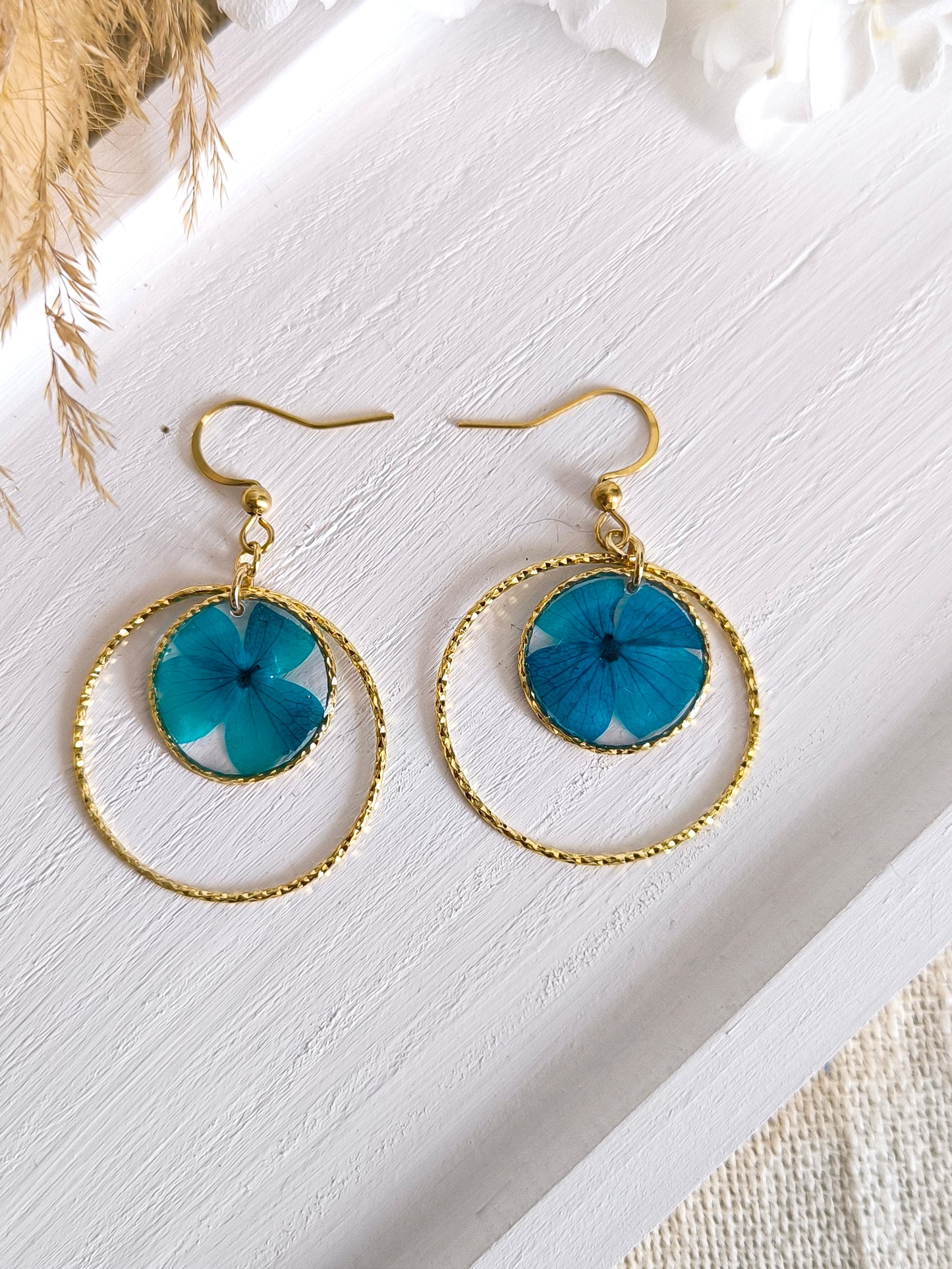 Boucles d'oreilles rondes avec fleur d'hortensia encapsulée dans une résine transparente.