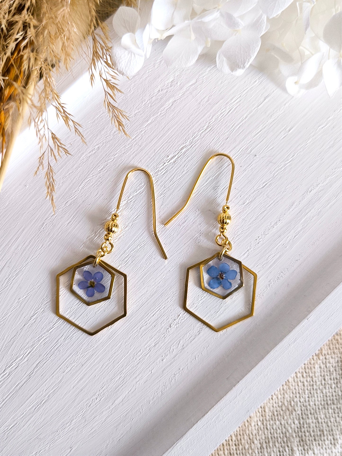 Boucles d'oreilles géométriques avec fleurs de myosotis et résine transparente.