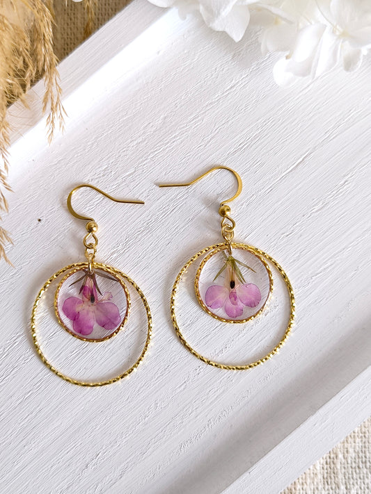 Boucles d'oreilles rondes avec fleur de lobélie encapsulée dans une résine transparente.